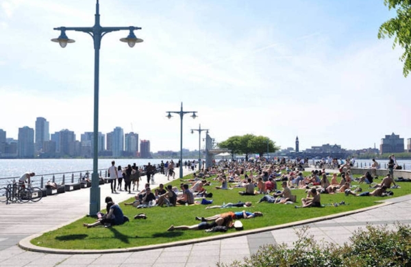 Vue sur le Hudson River Park, avec de nombreuses personnes assises sur l'herbe face à la rivière.